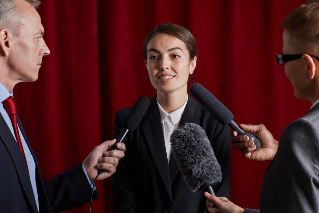 Portrait à la taille d'une jeune femme donnant une interview à un journaliste et parlant aux microphones contre un rideau rouge