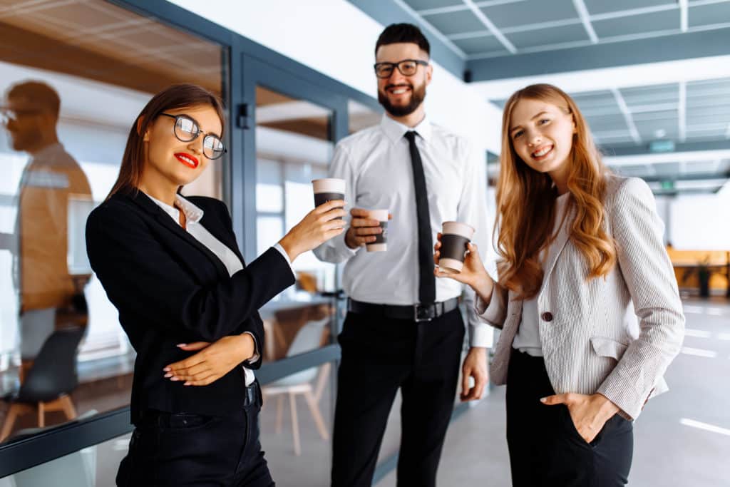 Jeunes gens d'affaires heureux debout et bavardant ensemble, tenant des tasses, dans un bureau moderne.